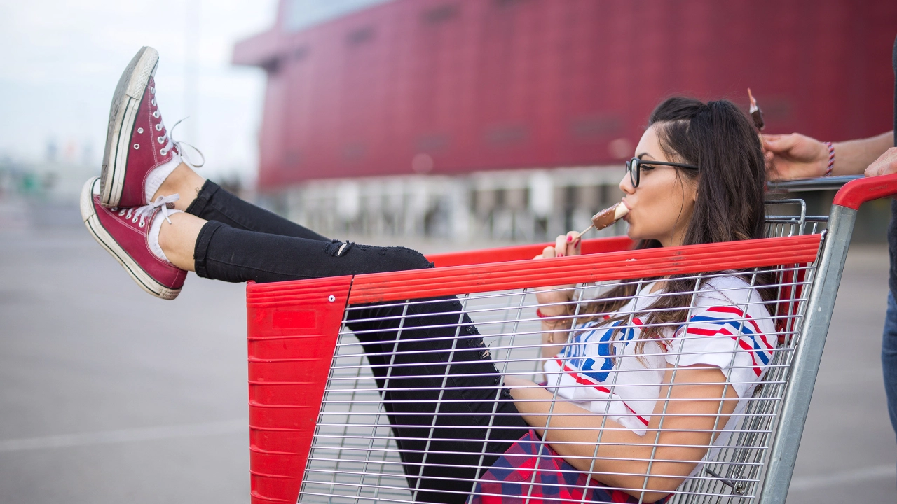 Mädchen sitzt lässig in einem Einkaufswagen und isst ein Eis