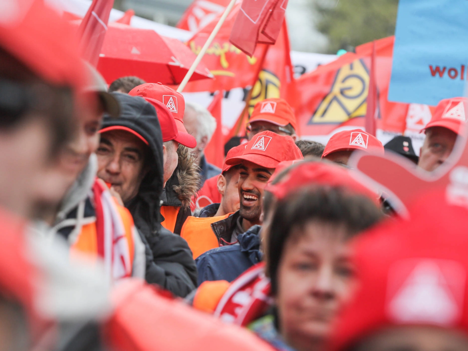Ein lachender Mann mit IG Metall-Kappe in einer Menschenmenge.