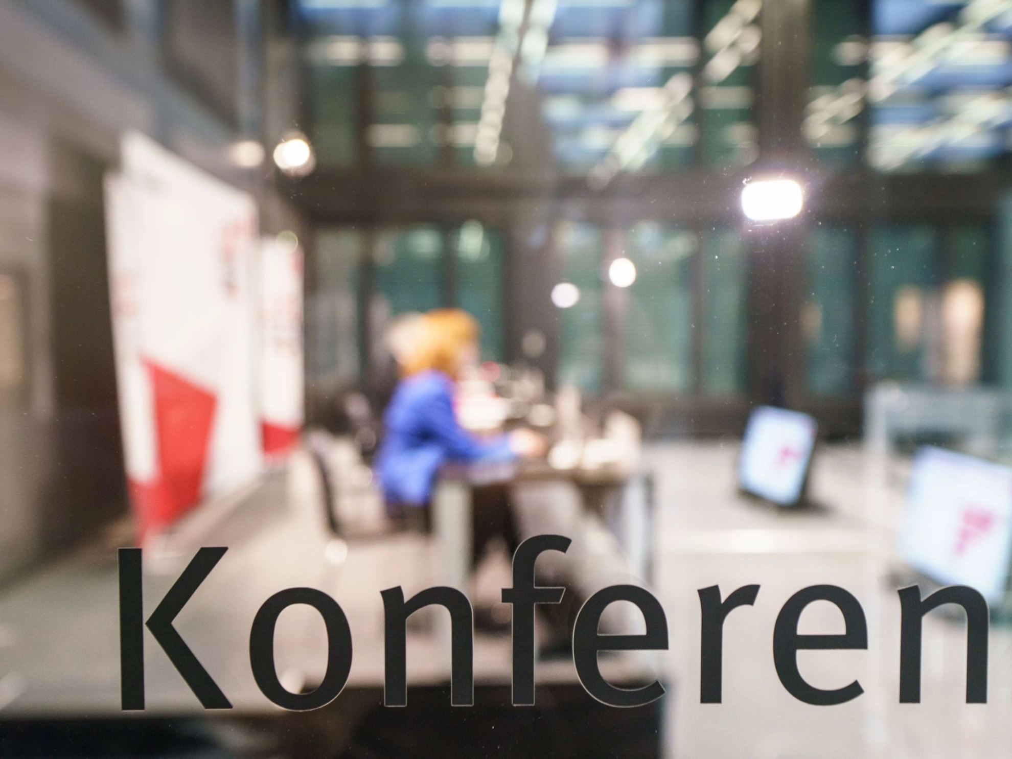 Glasscheibe mit der Aufschrift "Konferenz", dahinter unscharf ein Konferenzraum