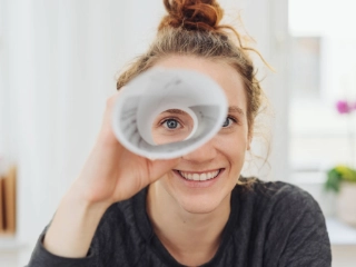 Eine junge Frau blickt durch ein gerolltes Blatt Papier.